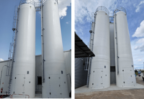 Installation de deux silos rigides industriels blancs côte à côte, équipés d’échelles, de passerelle et de tuyauterie, devant un bâtiment sous un ciel bleu.