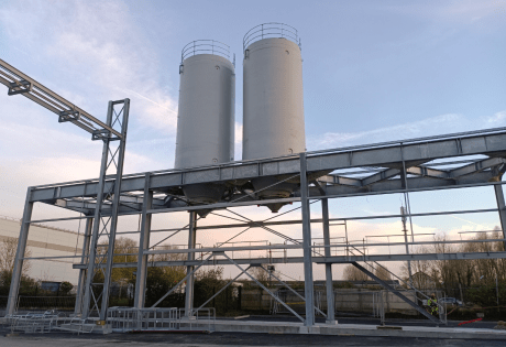 Deux silos rigides industriels blancs installés sur une charpente métallique extérieure avec passerelle et structure d’accès, photographiés au crépuscule sur un site de production.