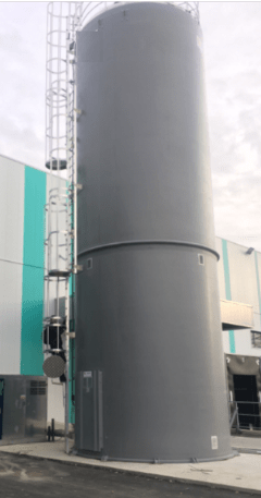 Silo rigide industriel gris anthracite équipé d’une échelle et d’un garde-corps en acier, installé devant une façade à panneaux blancs et turquoise.